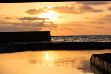 Coastal sunset on the Azores Island Santa Maria with a swimming pool in the foreground and the setting sun and clouds in the background, waves splashing