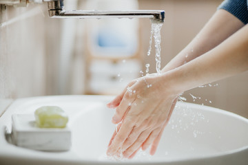 Closeup of a woman washing her hands in bathroom to prevent Covid-19 viral infection. Recommended washing with soap and running water during coronavirus pandemic. - obrazy, fototapety, plakaty