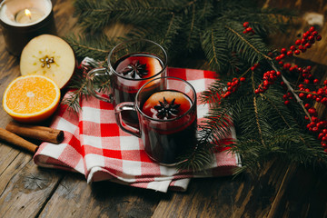 Two glass cups with mulled wine with citrus, apple and spices on checked tablecloth. Winter holiday...