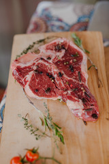 Wooden plate with raw T-bone steak with spices, cherry tomatoes, rosemary, coffe beans and sauce on a wooden plate.