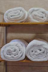 Obraz na płótnie Canvas Rolled white towels in a hotel bathroom wooden towel rack.