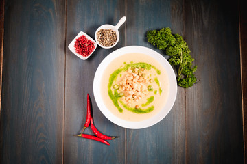 A plate of appetizing mushroom soup with croutons on a wooden table, among seasonings. Studio photography of food in the cooking industry, dark background.
