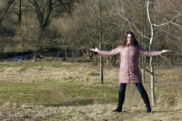 A girl is standing in a spring park. She spread her arms to the sides.