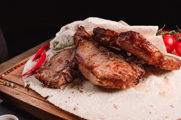 Appetizing fried meat lies on a wooden tray, among the seasonings. Studio photography of food in the cooking industry, dark background
