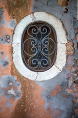 A small beautiful window on an old, historical wall with peeling paint.