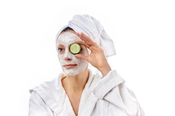Young beautiful girl with a white cosmetic mask on her face holds a cucumber in her hand.