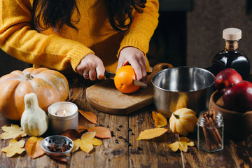 Close-up photo of woman in yellow sweater cutting orange for mulled wine. Autumn mood decorations...