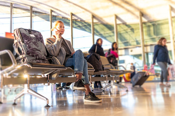 Casual blond young woman talking on cell phone while waiting to board a plane at bussy airport...