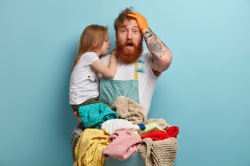 Obraz premium Dad and daughter prepare laundry for washing with detergent bottle. Frustrated father overloaded with domestic work, plays with small child, poses indoor. Household laundering. Weekend duties