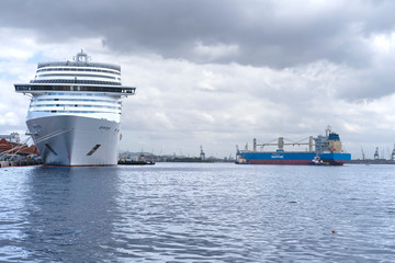 Cargo ship and large white ocean cruise liner stay in the port against the background of clouds. 