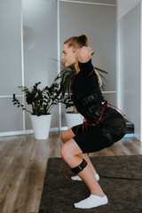 EMS training. Side view of girl doing squats in suit with cables.