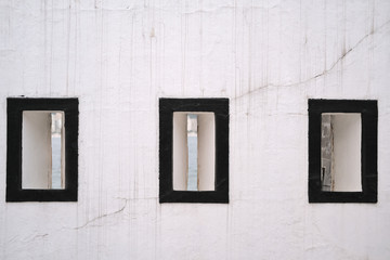 Obraz na płótnie Canvas Three windows with black border on a white wall with streaks and cracks. Ocean view through the windows.