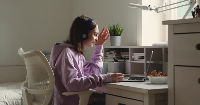 Teenage girl school student wearing wireless headphones conference calling on laptop distance learning at home. Teen schoolgirl chatting by web cam preparing for test or exam with online teacher.