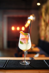 Delicious fruit alcohol cocktail in a  glass with ice, on the bar desk, warm bright lights in the background