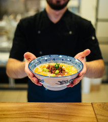 Delicious hot tantanmen ramen japanese noodle soup in a traditional blue bowl in male hands holding, upright