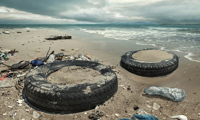 Car tire and plastic bottles pollution in muddy puddle on beach. (Environment concept)