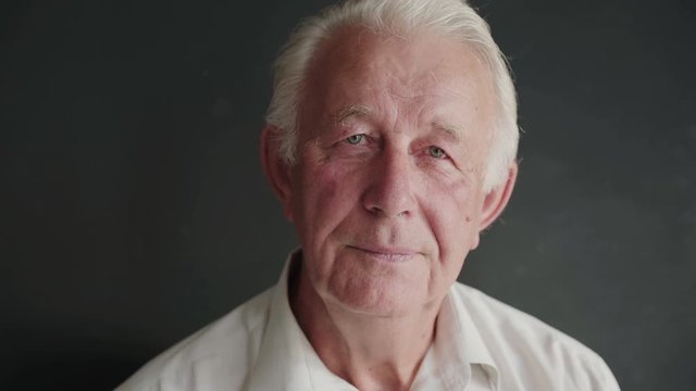 Portrait of senior man turns and looks with light smile at camera on background