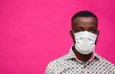 a young african doctor isolated over pink background wearing face mask to prevent himself from the...