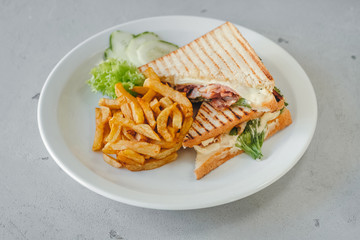 Horizontal close-up photo of club sandwich with fries and vegetables on a white plate. Meal time.