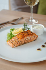 Beautifully served salmon fish steak and a glass of white wine. Crispy grilled salmon steak with lemon, salad and rosemary.
