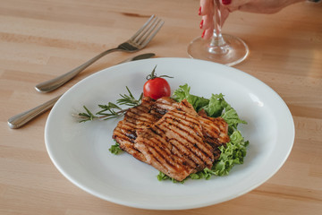 Grilled chicken steak with salad, cherry tomato and rosemary on a plate in a restaurant. Concept of eating out.