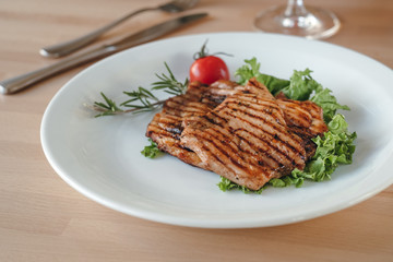 Grilled chicken steak with salad, cherry tomato and rosemary on a plate in a restaurant. Concept of eating out.