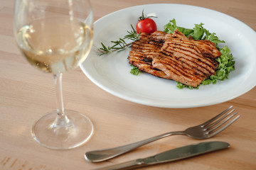 Grilled chicken steak with salad, cherry tomato and rosemary on a plate in a restaurant. Concept of eating out.