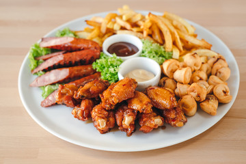 Close-up of large hot beer plate with sausages, fries, chicken and sauses.