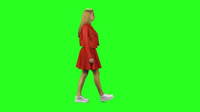 Blonde girl calmly walking on green screen background. Chroma key, 4k shot. Profile view.