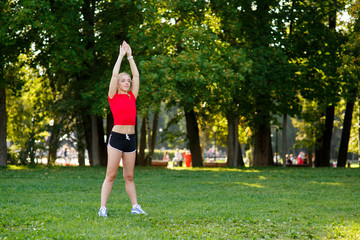 A young blonde girl is engaged in sports in the park, a woman does a warm-up in the street. Active outdoor training