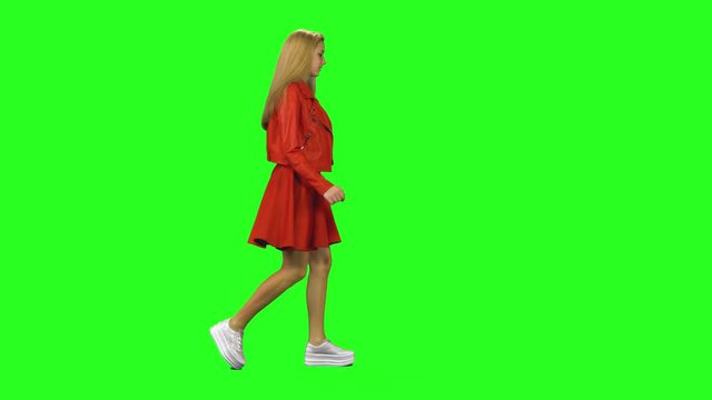 Blonde girl is running to a meeting with lovely smile at green screen background. Chroma key, 4k shot. Profile view.