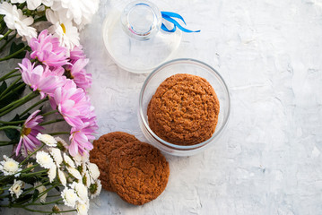 Oatmeal cookies in a glass jar. Bouquet of flowers. Tender woman composition on a gray background Top view.