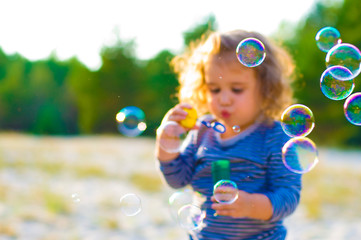 horizontal defocused photo of funny curly-haired girl with soap bubbles