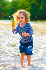 vertical photo of a little curly girl with soap bubbles on the beach