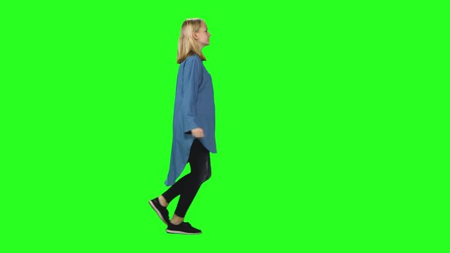 Blonde teenager girl is running with smile at green screen. Chroma key, 4k shot. Profile view.