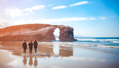 Three young women walking on Cathedrals Beach in Galicia
