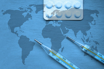 Top view on two thermometers and white tablets on a world map background
