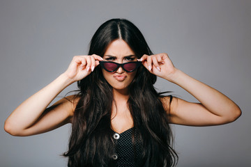 Beautiful young woman in sunglasses looking angry at camera on grey background.