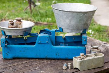 Old-fashioned scales for weighing fruits and vegetables, rusty weights or old breasts weights are on ancient balance scales. Against the backdrop of a vegetable garden, an agricultural yard, old table