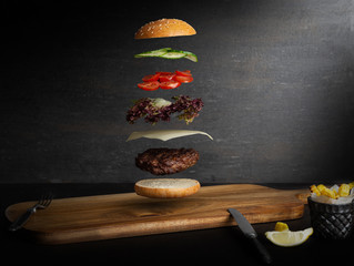 Burger mięsny z latającymi składnikami, na białym tle, z miejscem na tekst lub logo, czarne tło i jasne kolory - 333680960