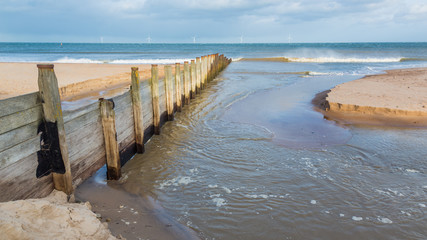 Meggies Burn, a small river leaving the beach and flowing into the sea after being re-routed underneath a wooden groyne by a storm. Blyth Beach, Northumberland, England, UK.