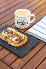 Crispy cereal toast with peanut butter, bananas, chocolate and a caffe latte on the wooden breakfast table.