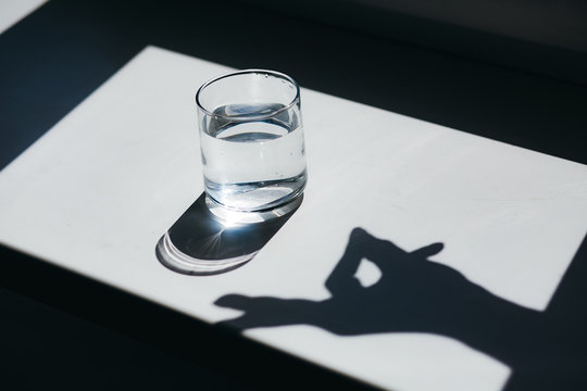 Water glass with strong shadows and hand gesture silhouette on white background