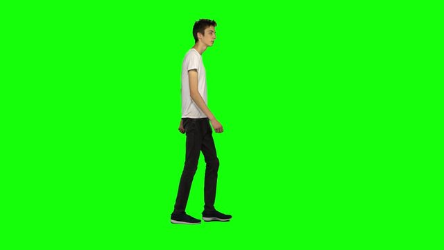 Tall skinny teen guy calmly walking on green screen background. Chroma key, 4k shot. Profile view.