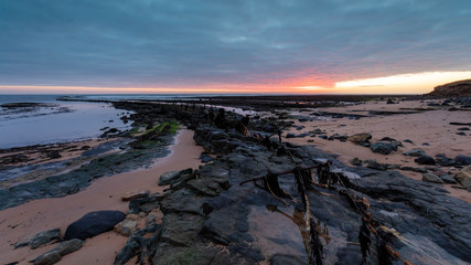 Fototapeta na wymiar The fence to nowhere. A wire fence on rocks at Boulmer on the coast of Northumberland, England, UK. At sunrise.