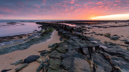 The fence to nowhere.  A wire fence on rocks at Boulmer on the coast of Northumberland, England,...