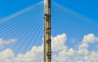 Bridge tower and suspender cables with a background of blue sky and clouds.