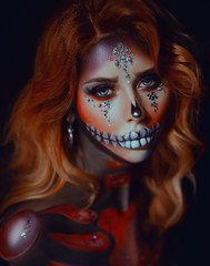 Closeup portrait young woman with art makeup sugar skull. Ancient fashionable vintage traditions modern world. Red wavy hair. Goddess death decorated bright shiny sparkling rhinestones. Feast of Dead