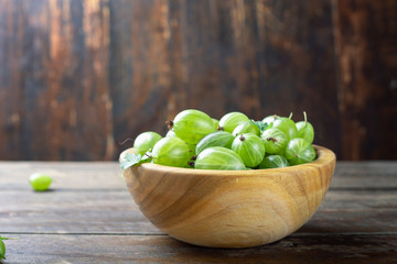 Sweet fresh gooseberry berry in a bowl on wood background.