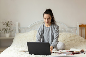 Young girl woman on the bed, distance learning for students. Coronavirus. Quarantine. Woman look at a laptop computer. Freelancer, distant work, work at home, online education